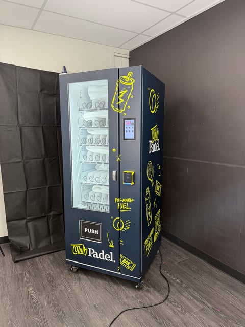 Wildly Padel branded vending machine with blue and yellow design, stocked with merchandise behind glass doors in an indoor space