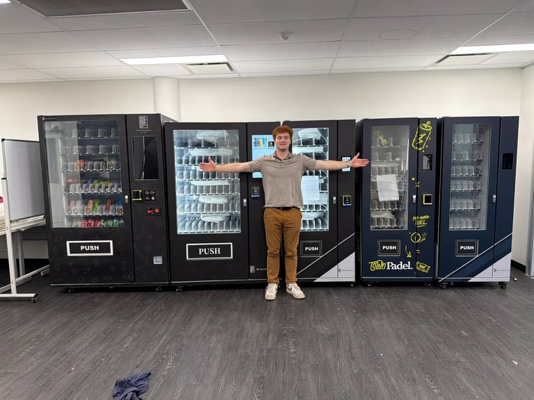 Person standing in front of a row of vending machines with arms outstretched in an office or break room setting