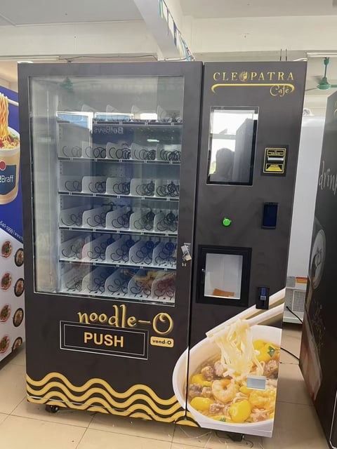 Black and gold noodle vending machine with illuminated product display and cup dispenser in bottom shelf