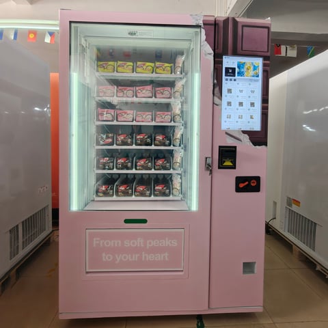 Pink vending machine with frozen treats displayed behind illuminated glass door, payment panel on right side