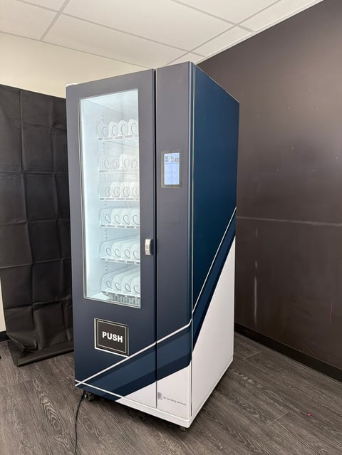 Modern blue and white vending machine with glass front door displaying products on shelves, located indoors
